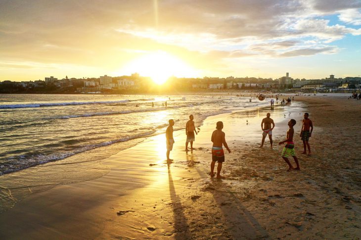 Folk leger på stranden med fodbold i solnedgang